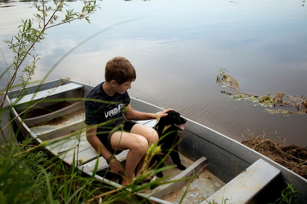 A Young Boy Sitting on a Wooden Boat with His Dog. Naturopath Caloundra