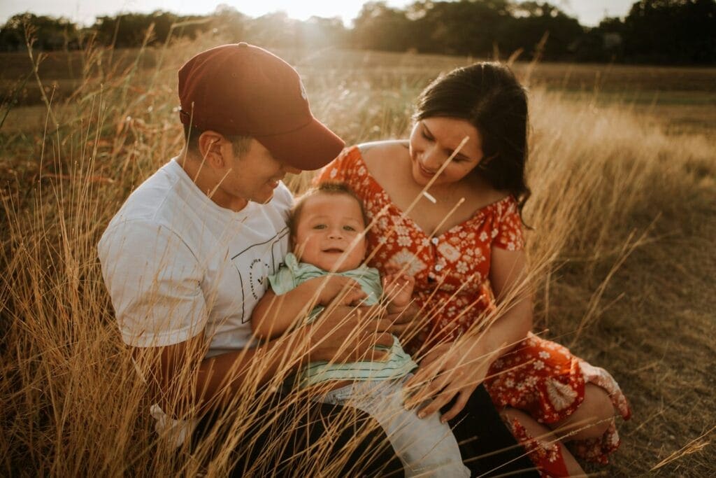 Man and woman sitting in a grass field with their baby. Naturopath near me. Infant colic natural remedies. Colic in babies