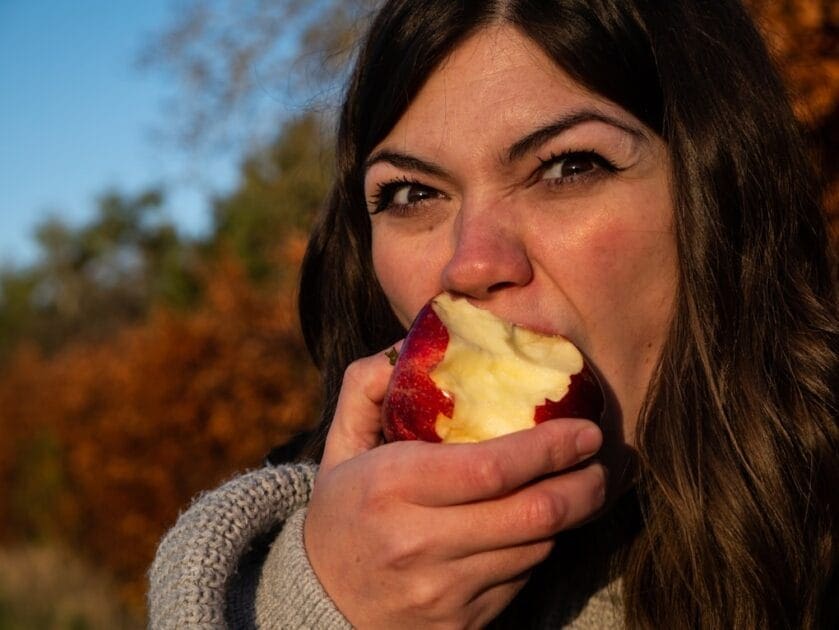 Woman in gray sweater eating an apple. Gut Health Brisbane