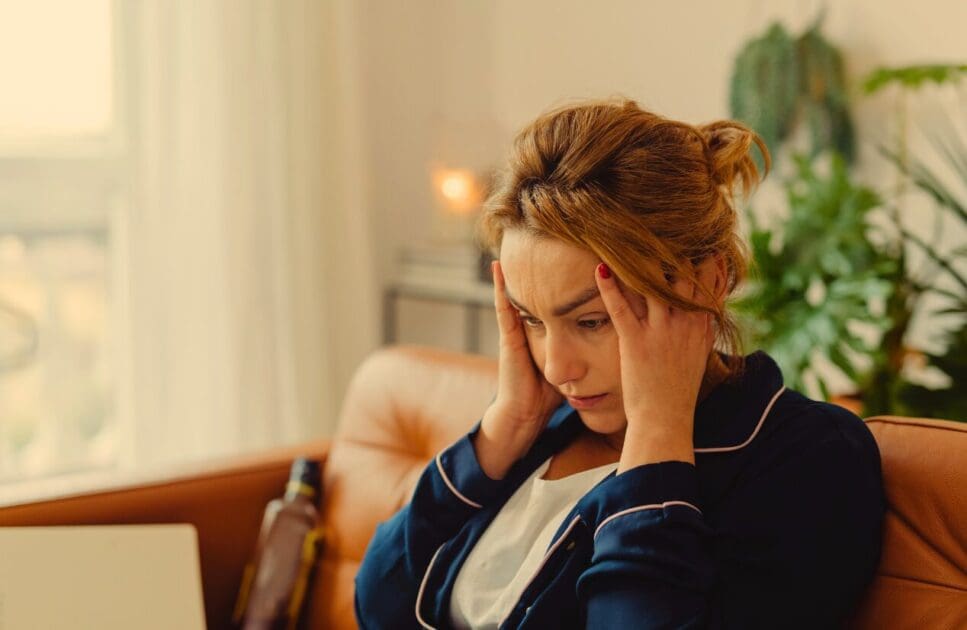 Woman sitting on a couch with her head in her hands. Dealing with Adrenal Fatigue. Stress and how it manifests. Stress. Counselling for Adults Who Are Tired of Pretending. Brisbane Livewell Clinic