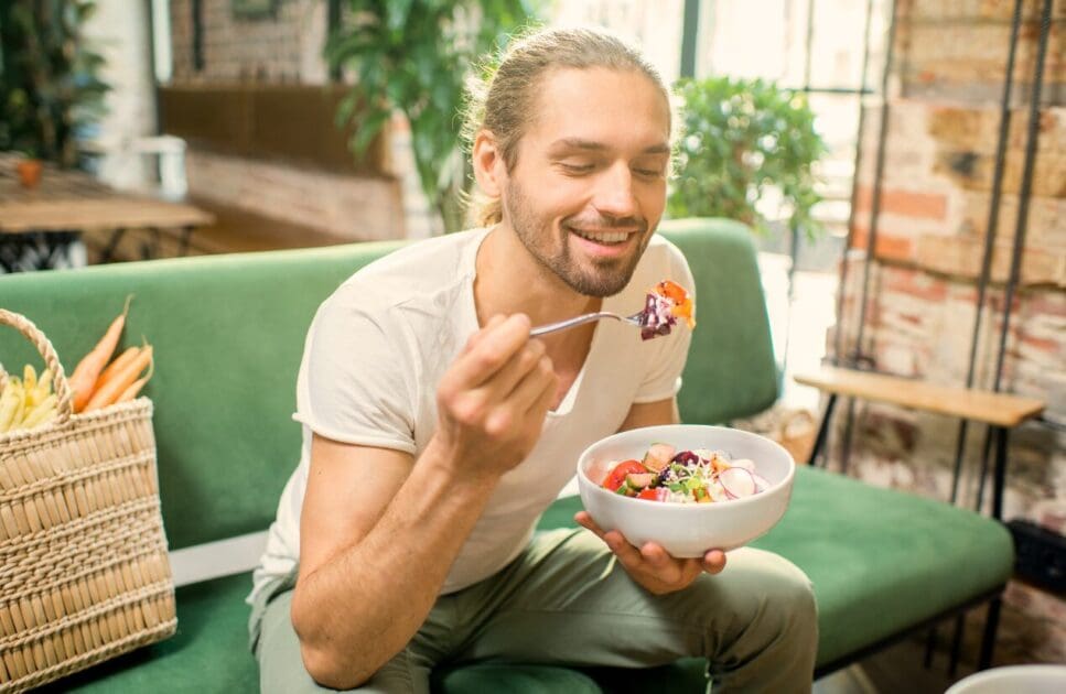 Man sitting on a couch while eating fresh salad. Mood & Food. What is Gut Health Australia? Healthy food and healthy diet. Clinical Nutritionist Cannon Hill. Nutritionist Brisbane. Brisbane Livewell Clinic