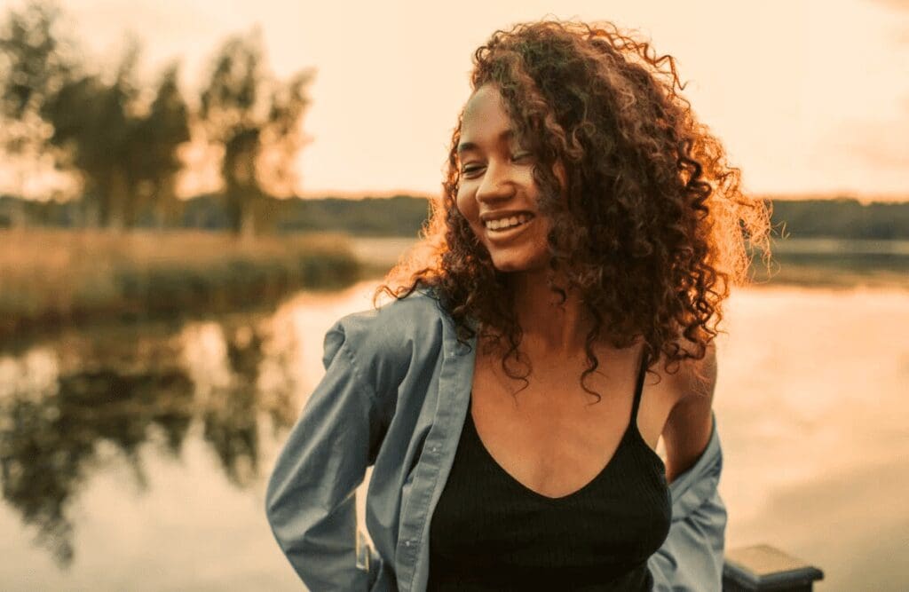 Smiling woman standing outdoors near a lake. Hypnosis Therapy in Melbourne. How Osteopathy may Support Posture and Structural Alignment. Brisbane Livewell Clinic