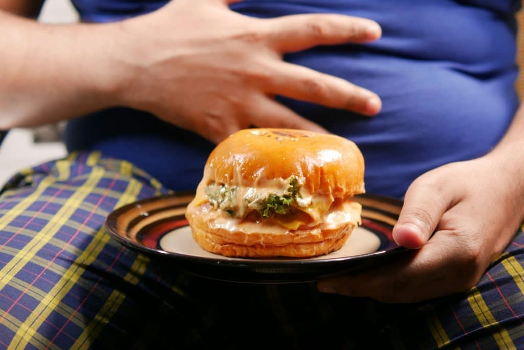 A person holding a plate with a burger on it. Digestive problems that cause weight gain