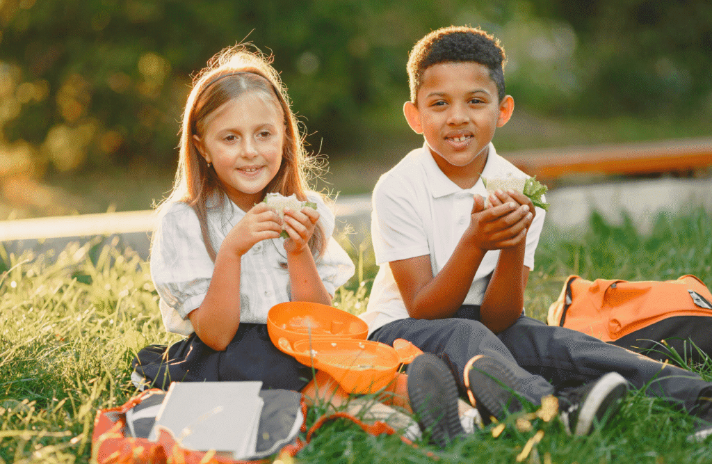 Two children sitting on the grass, eating their snacks together. Mood & Food. Naturopath for Children. Clinical Nutritionist Camp Hill. Brisbane Livewell Clinic