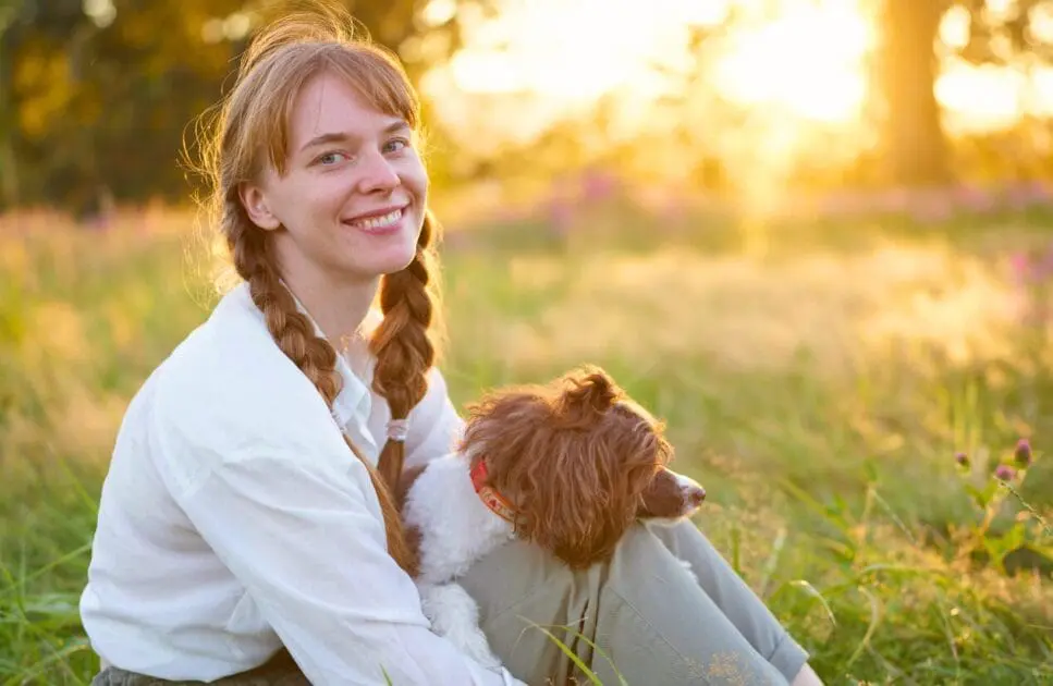 Woman sitting in the grass with her dog, enjoying a sunny day outdoors. Hypnotherapy near Hendra. Naturopath Blood Test. Burnout Holistic Counselling. Brisbane Livewell Clinic