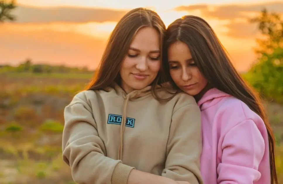 Two young women share a heartfelt hug outdoors during a beautiful sunset. Hypnotherapy near Chermside. I Don't Feel Like I Belong Anywhere. Hypnotist Near Me. Brisbane Livewell Clinic
