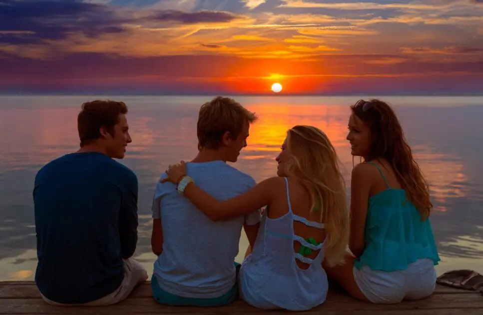 Four friends sitting on a wooden dock, enjoying the beautiful sunset over the calm water. Massage Near Me. Methylation Near Me. Hypnotist Near Me. Bribsane Livewell Clinic.