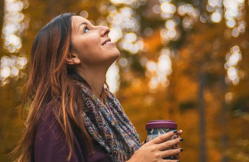 Woman holding a cup of coffee and looking up at an autumn forest. Clinical Hypnotherapy. Brisbane Livewell Clinic