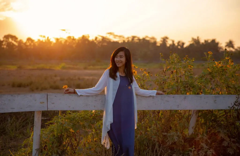 Smiling woman standing by a wooden fence. Naturopath Cannon Hill. Osteopathy for Hip Pain and Pelvic Imbalance. Osteopath for Sciatica. Brisbane Livewell Clinic
