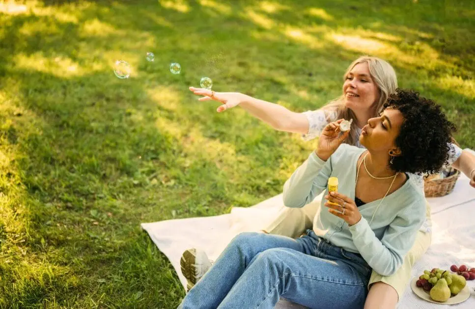 Two women sitting on the grass, playfully blowing bubbles. Hypnotherapy near Nundah. Relationship Counseling Near Me. Holistic Counselling North Brisbane. Brisbane Livewell Clinic