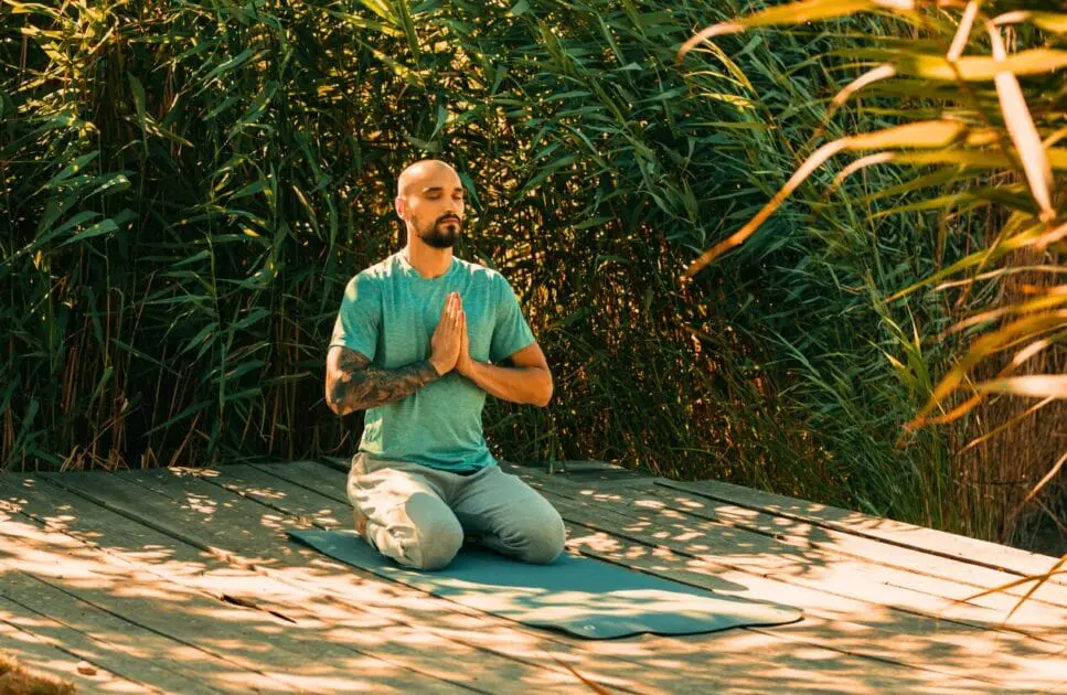 A young bearded man meditating on a wooden platform by the lake. Hypnotherapy near Stafford Heights. Brisbane Livewell Clinic