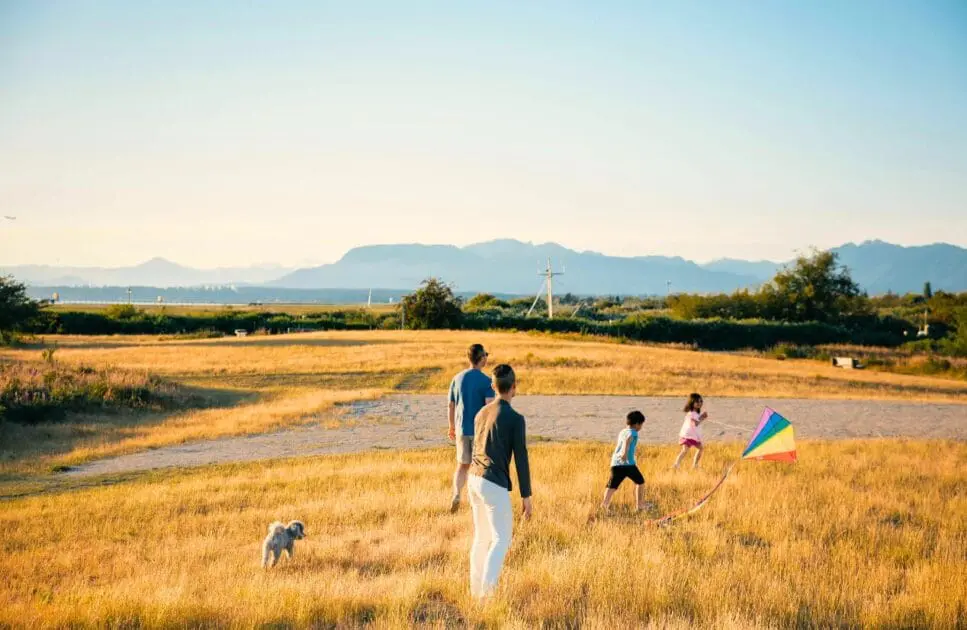 Two adults and two kids having fun playing with kite in the grass field. Hypnotherapy near Northgate. Brisbane Livewell Clinic