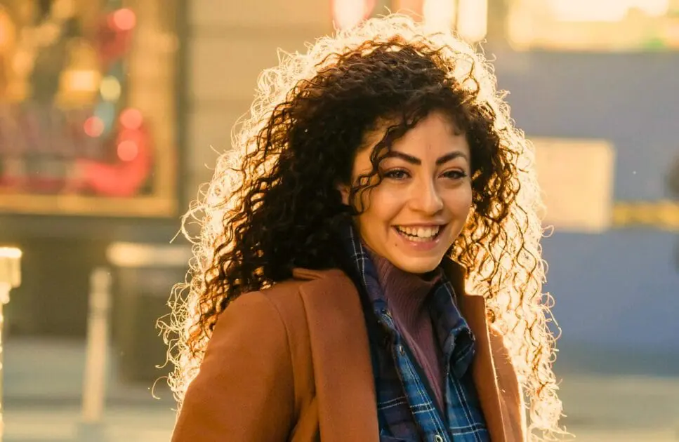 Woman with curly hair smiles warmly while standing on a bustling street. Hypnotherapy near Gordon Park. Bowen Therapy in Brisbane. Brisbane Livewell Clinic