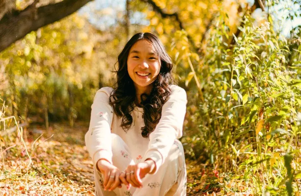 Smiling woman sitting on the grass. Hypnotherapy near Clayfield. Hypnotherapy. Mindset Therapy Brisbane. Osteopath for Lower Back Pain. Pyrrole Disorder. Brisbane Livewell Clinic